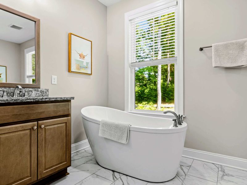 Primary Bathroom - Freestanding soaking tub by a sunny window, vanity reflected in the framed mirror.