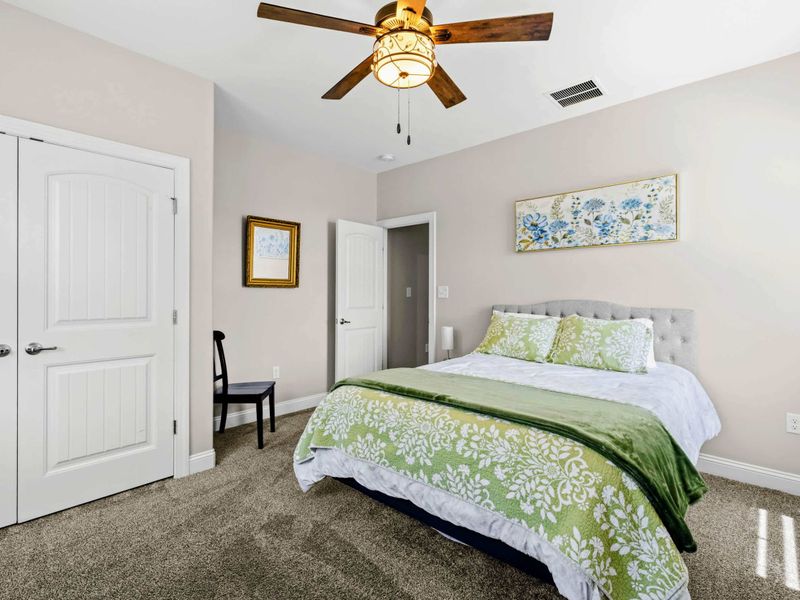 Bedroom 2 - Tufted gray headboard, floral art above the bed, and crisp green-patterned bedding.