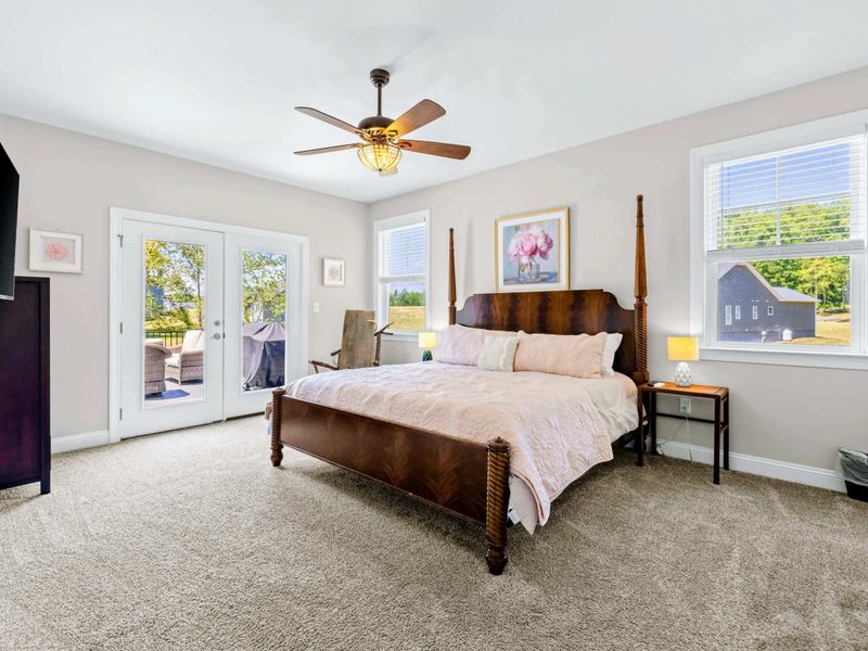 Primary Suite - King four-poster bed with peach quilting, ceiling fan, and French doors leading straight to the deck.