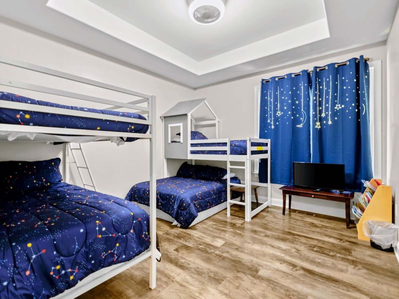 Bunk Room - Two bunk sets plus a house-frame loft bed with constellation bedding, a TV, and star-pattern blackout curtains. Kid heaven.