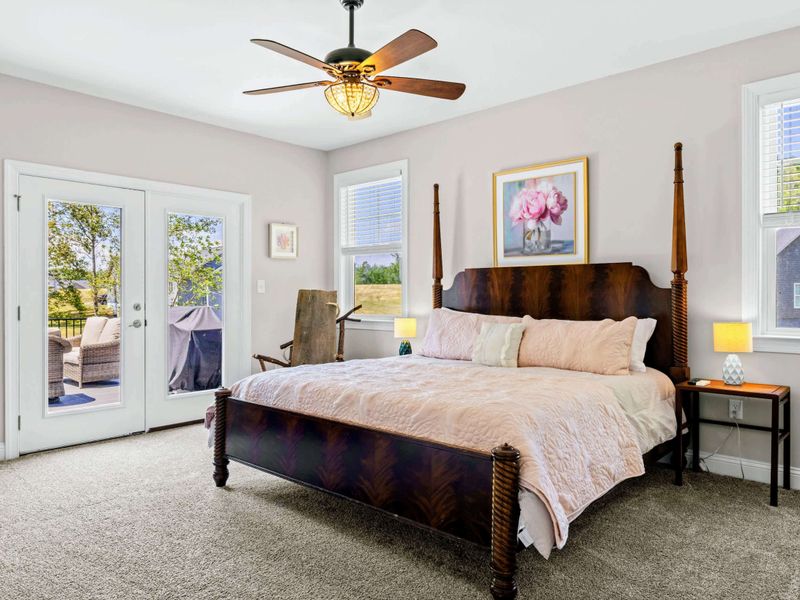 Primary Suite - Carved wood four-poster bed, plush blush bedding, and a quiet seating nook by the French doors.