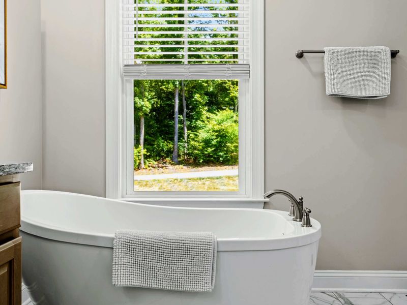 Primary Bathroom - Soaking tub close-up with a folded towel and forest view through the window.