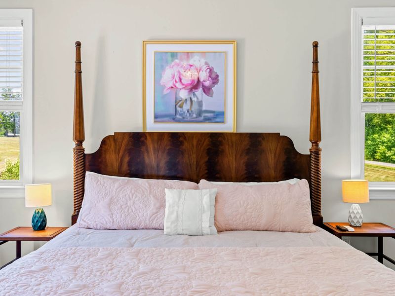Primary Suite - Detail of the four-poster headboard with peony art above and matching nightstand lamps.