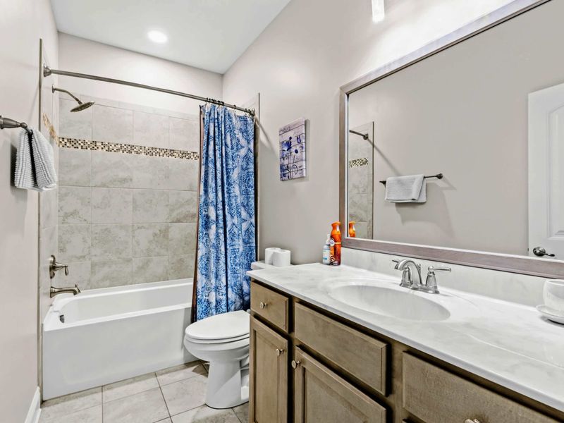 Bathroom - Tile-surround tub-shower with a mosaic accent stripe and granite-look vanity counter.