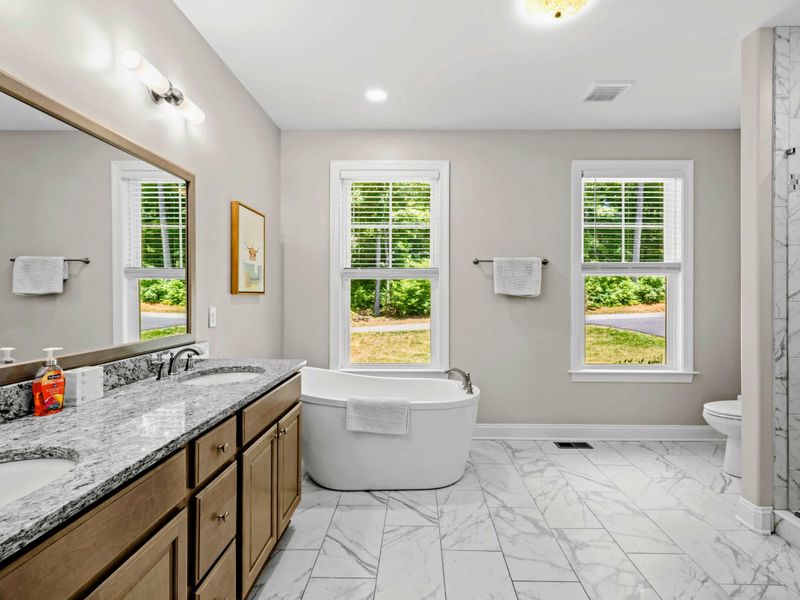 Primary Bathroom - Marble-tile floors, granite-topped double vanity, freestanding soaking tub, and walk-in shower come together for a spa-like retreat.