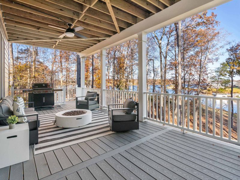 Fire Pit Deck - A white fire pit, wicker seating, and a propane grill anchor the lower deck, with lake views just beyond the railing.