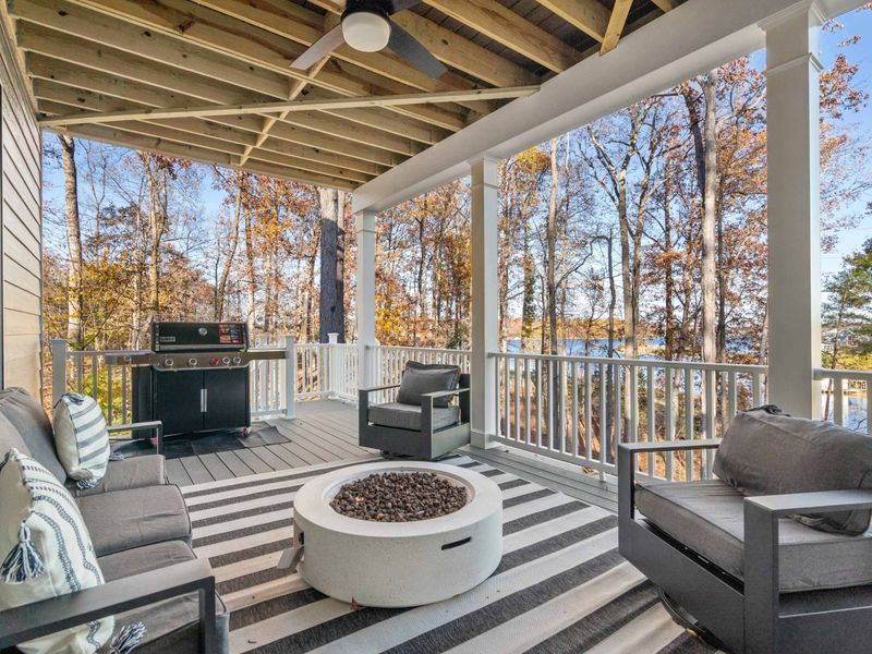 Lakeside Fire Pit - The lower deck fire pit area with cushioned seating, a grill, and a clear sightline to the water.