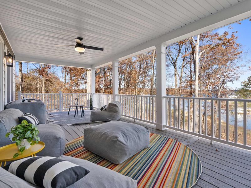 Upper Deck Lounge - Plush gray seating, striped pillows, and a colorful area rug on the covered wraparound porch with lake views.