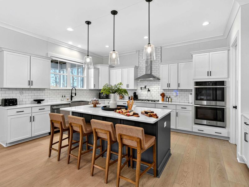 Kitchen Overview - White cabinetry, quartz countertops, a dark island, and stainless steel appliances including a double wall oven.