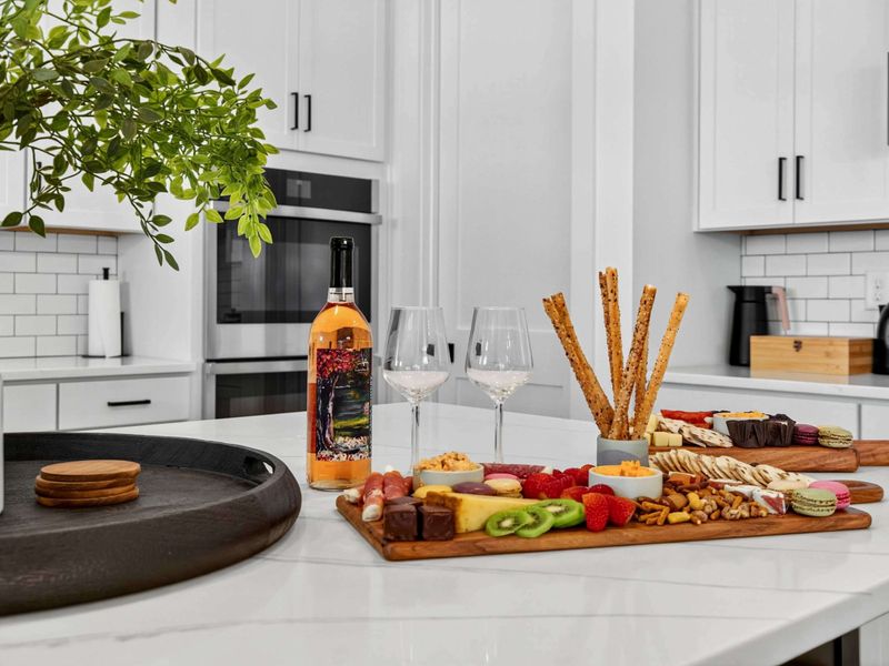 Kitchen Detail - Wine, charcuterie, and a cake stand on the island, with the double wall oven and subway tile in the background.