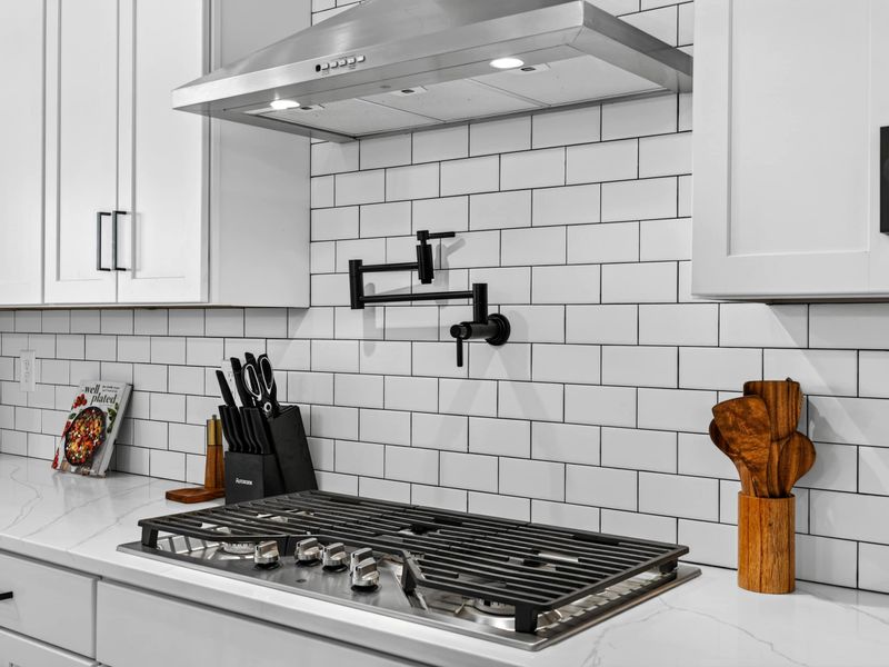 Pot Filler and Cooktop - The matte black pot filler mounted above the gas range, with wooden utensils and a cookbook nearby.
