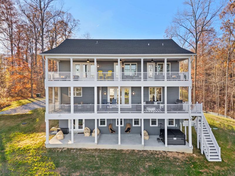 Aerial Rear View - All three levels of covered porches, the hot tub, swing chairs, and green yard leading down to the water.