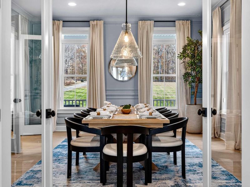Formal Dining Room - A set table for eight behind French doors, with blue-gray wainscoting, pendant lights, and views of the front yard.