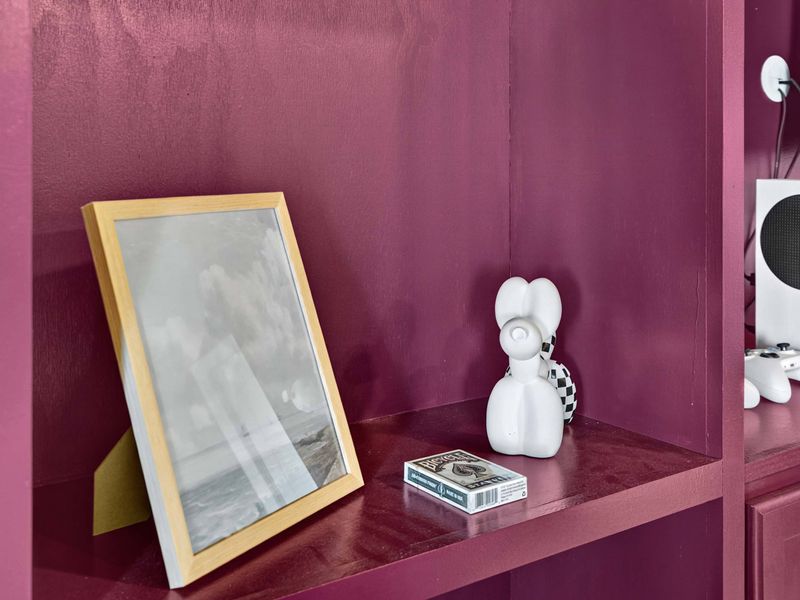 Shelf Detail - A framed print, a decorative sculpture, and an Xbox console on the plum-painted entertainment shelves.