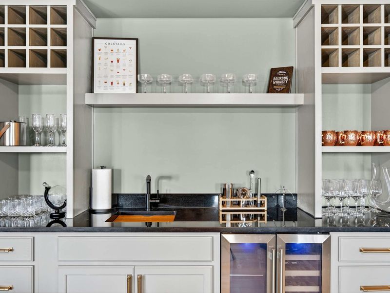 Wet Bar - A full bar setup with dual wine fridges, a cocktail guide, copper mugs, stemware, and a black granite countertop.