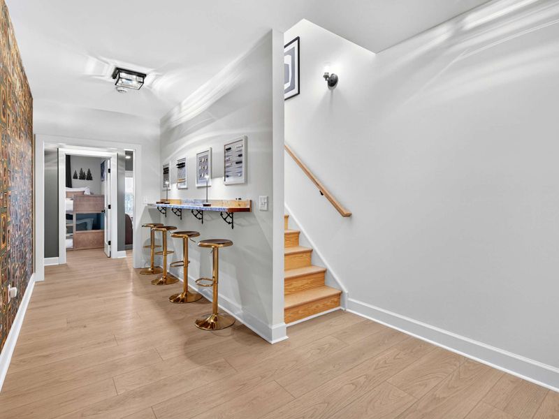 Lower Level Hallway - The game bar, gold stools, and accent wallpaper lead to the lounge and bedrooms, with stairs up to the main level.