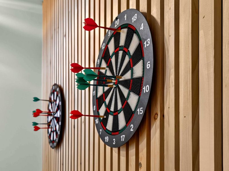 Dart Close-Up - Red and green darts clustered on the board, with the slatted wood wall adding texture and warmth.