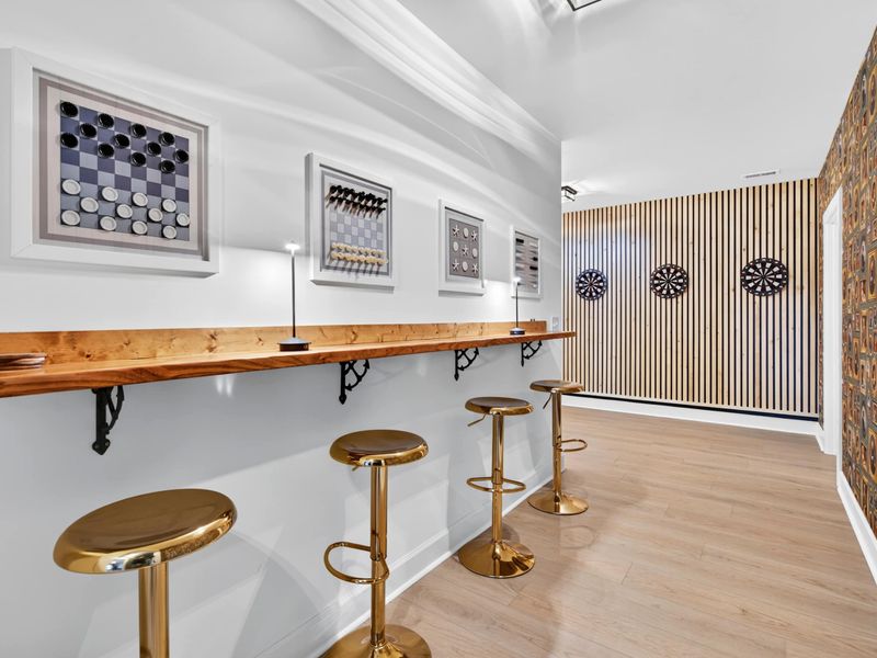 Game Bar Wide - The full game bar with brass stools, wall art, dartboards, and the accent wallpaper tying it all together.