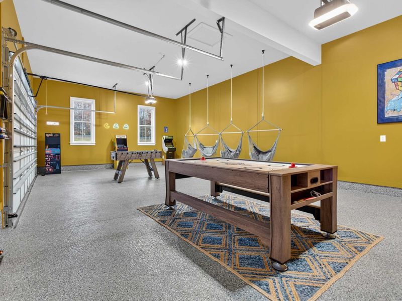 Game Room Wide View - Air hockey, hanging hammock chairs, foosball, and arcade games fill the garage-level entertainment space.