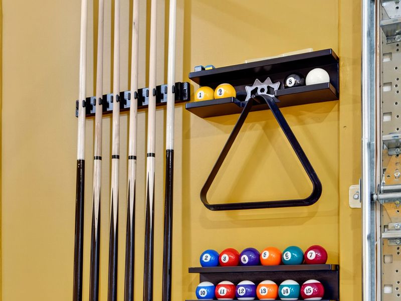 Pool Cue Rack - Cues, a triangle rack, and a full set of billiard balls mounted on the wall, ready for a game.