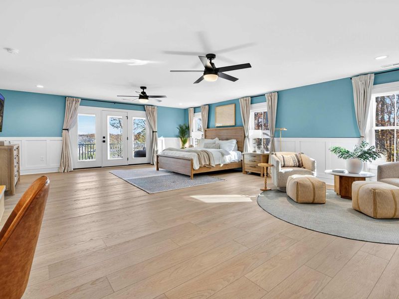 Primary Suite - A sprawling retreat with a king bed, sitting area, French doors to the deck, and blue walls with white wainscoting.