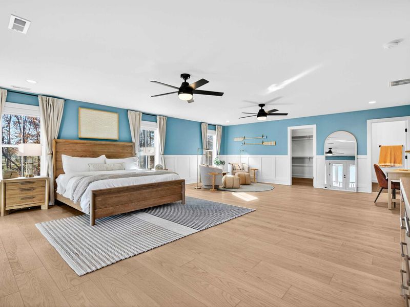 Primary Suite Bed View - The king bed flanked by windows, with the walk-in closet, ensuite, and desk visible across the room.
