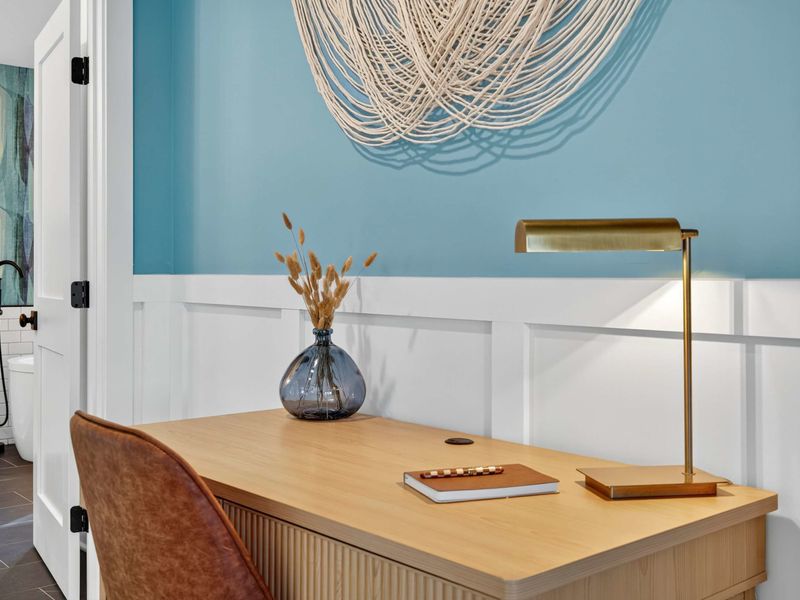 Primary Desk - A ribbed oak desk with a leather chair and brass lamp, tucked near the ensuite bath entrance.
