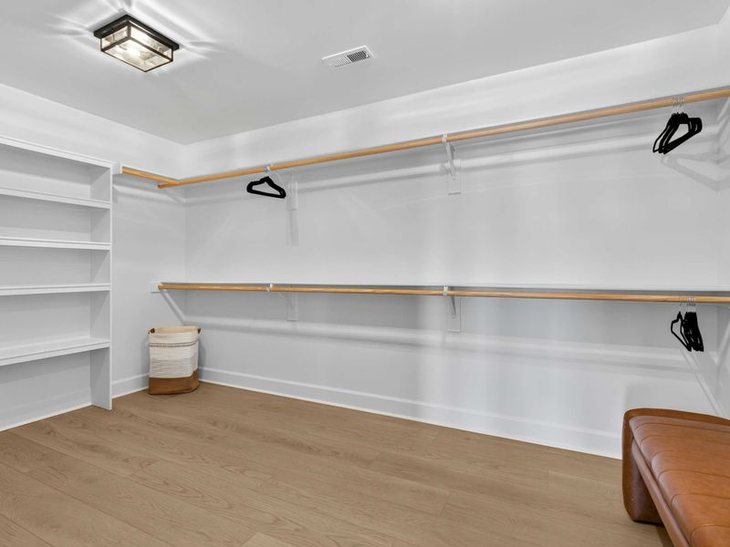 Walk-In Closet - A generous walk-in closet with double hanging rods, built-in shelving, and a leather bench.