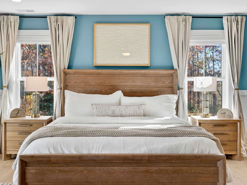 Primary Bed Detail - The oak king bed with crisp white linens, a knit throw, and matching nightstands flanked by windows.