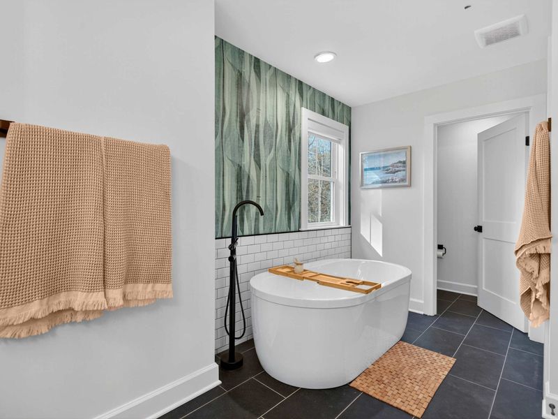 Primary Soaking Tub - A freestanding soaking tub with a bamboo caddy, green botanical wallpaper, subway tile, and a matte black faucet.