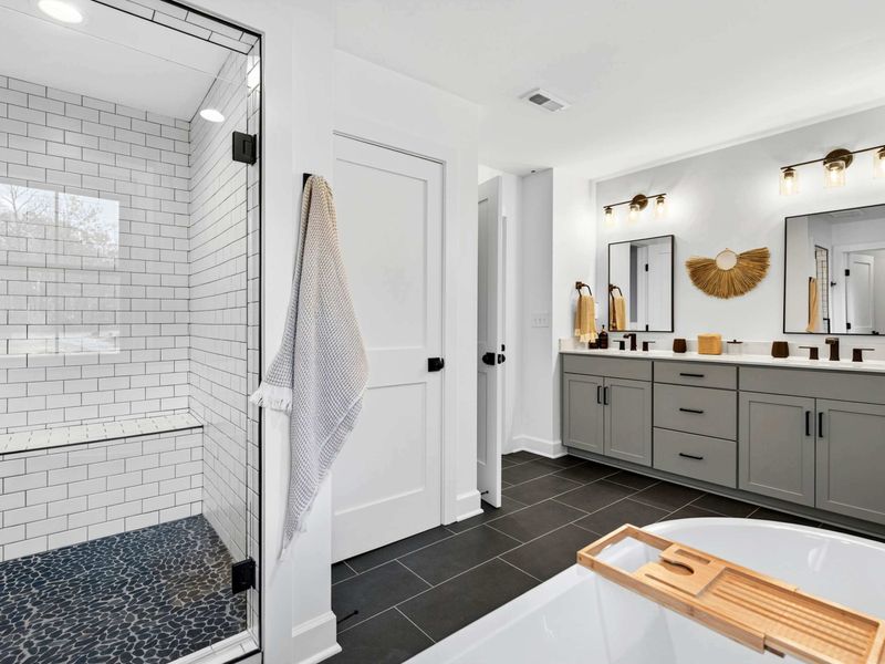 Primary Shower and Vanity - A glass-enclosed walk-in shower with pebble floor, subway tile, and the double vanity beyond.