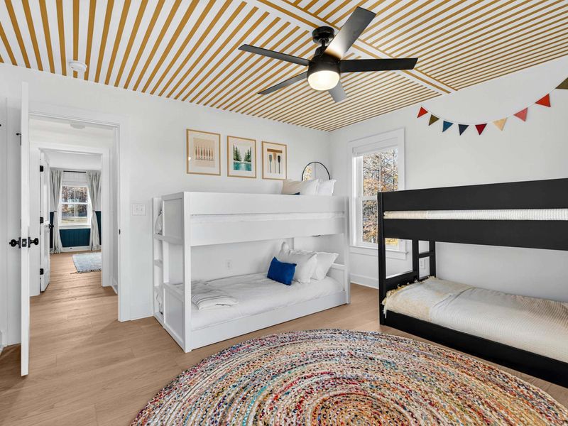 Bunk Room Wide View - Both bunk beds visible with playful art, the striped ceiling detail, and a doorway to the bathroom.