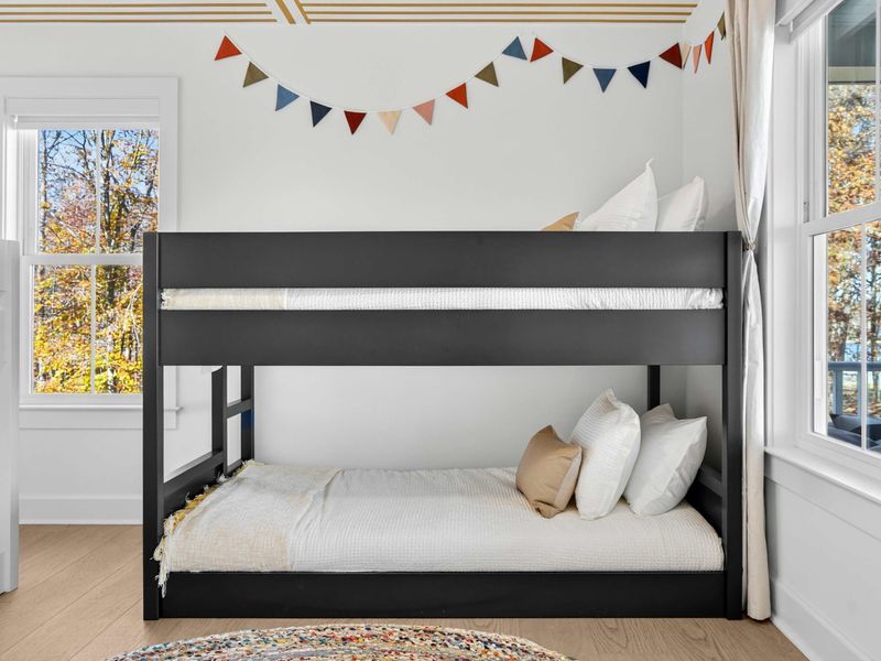 Black Bunk Close-Up - The full-over-full black bunk with colorful triangle bunting, autumn tree views, and a braided rug below.