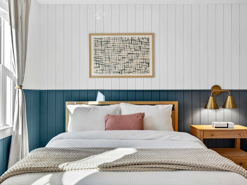 Bed Detail - Abstract art and brass sconces add a refined touch to the navy wainscot accent wall.
