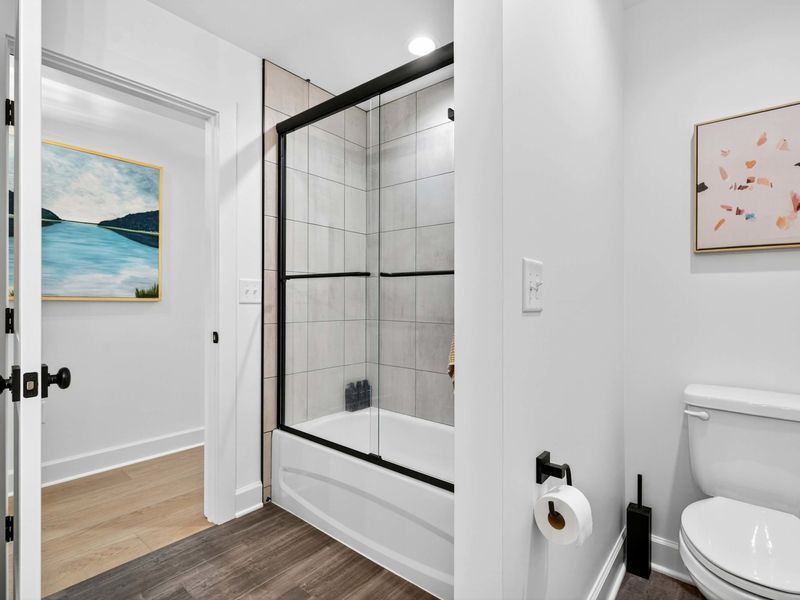 Shared Bath - A tub and shower combo with black-framed glass doors and gray tile, plus a lake painting in the hallway.