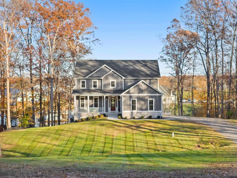 Property View - A wider angle showing the home set among mature trees with a spacious yard and driveway.