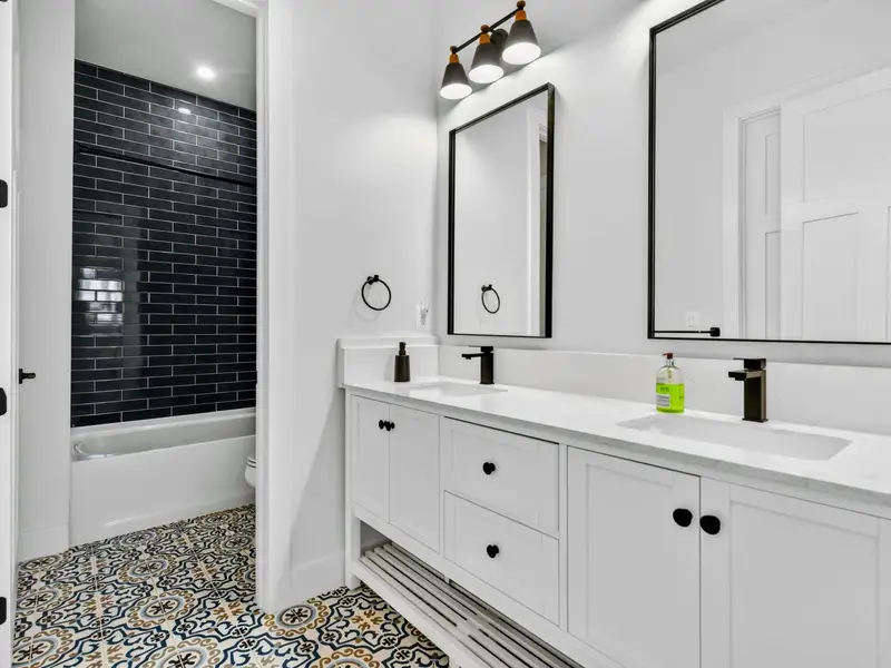Lower Bath 4 - A double vanity with ornate patterned floor tile, black fixtures, and the tub-shower beyond.