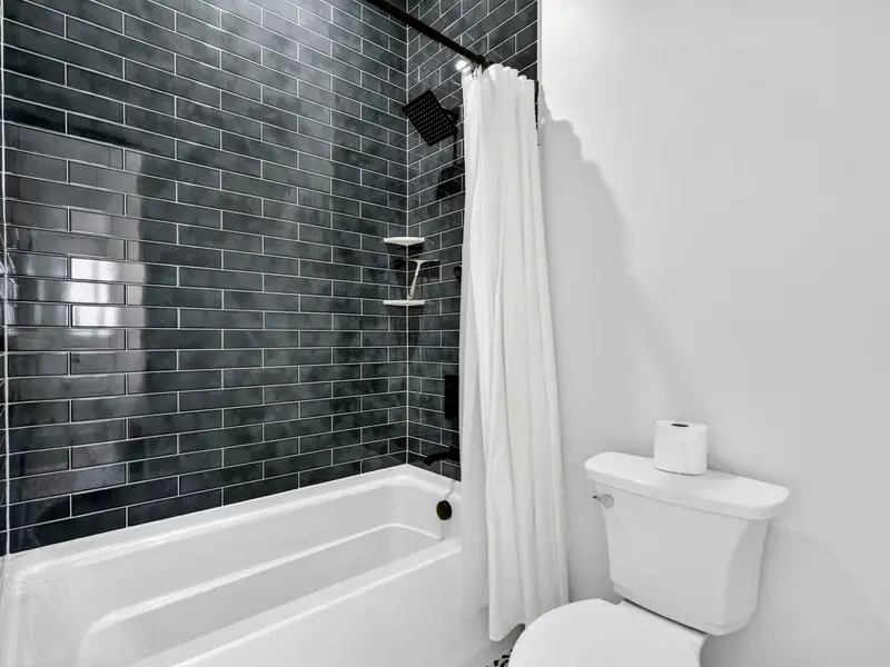 Lower Bath 4 Tub - Dark subway tile surrounds the tub-shower combo, with a rainfall head and white curtain.