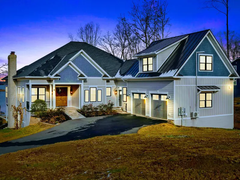 Twilight Exterior - The craftsman facade glows with warm light at dusk, with the stone chimney and metal roof accent on display.