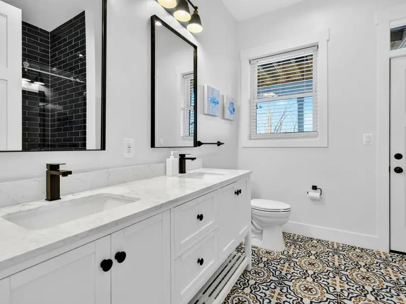 Lower Bath - A double vanity with hand-painted Moroccan floor tile, matte black fixtures, and a glossy dark shower beyond.