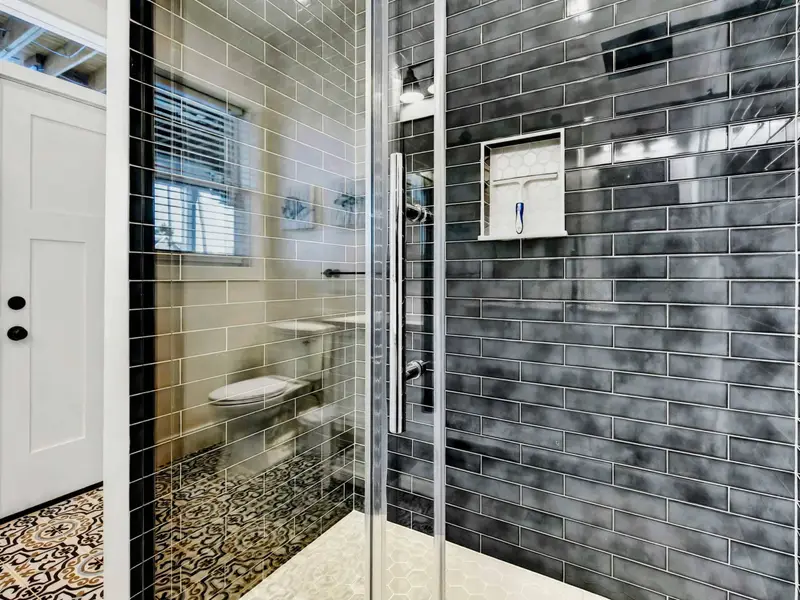 Shower Detail - Glossy charcoal subway tile and a glass enclosure line the walk-in shower in the lower bath.