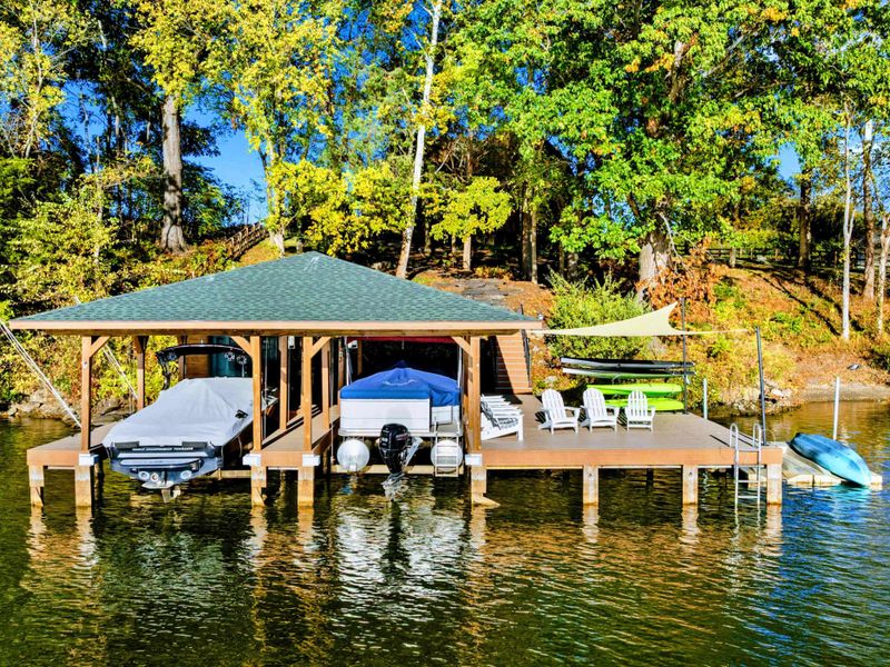 Aerial - The covered boathouse and open dock extend into the lake with the wooded hillside rising behind.