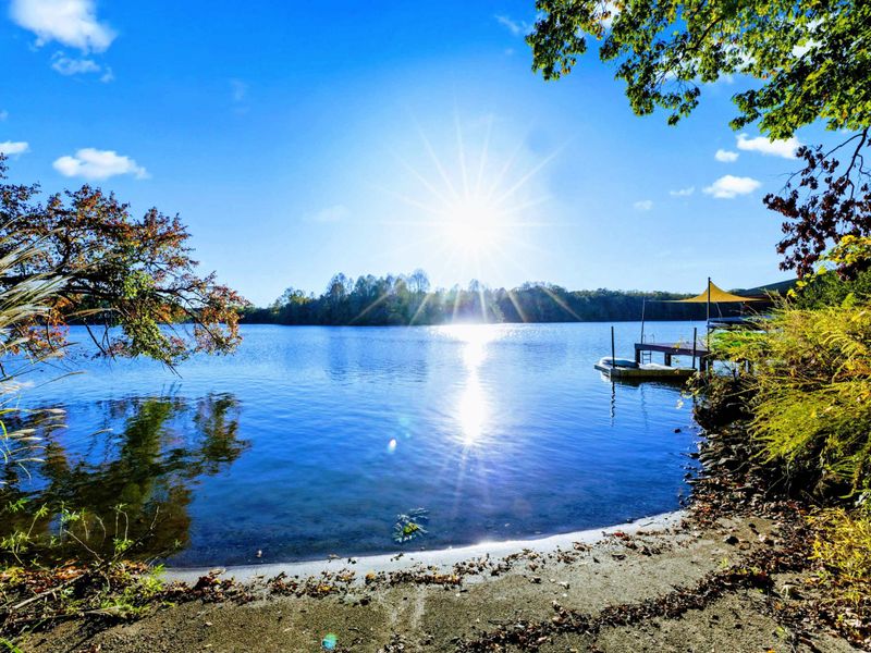 Waterfront - Sun bursts through the trees over crystal-clear water, with the dock and kayaks ready for the day.