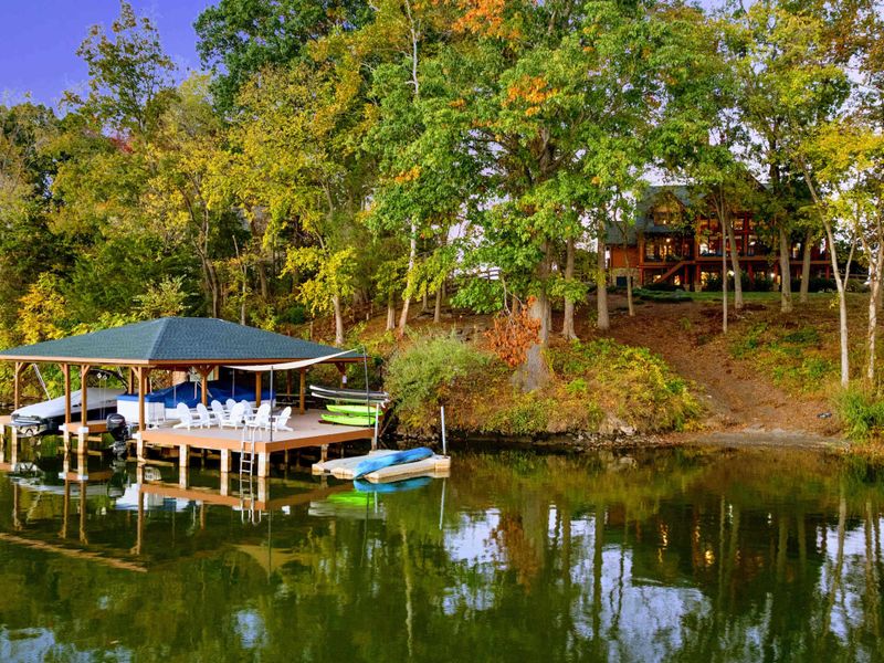 Aerial - Full waterfront view showing the dock, boathouse, kayaks, and the log home perched among the trees above.