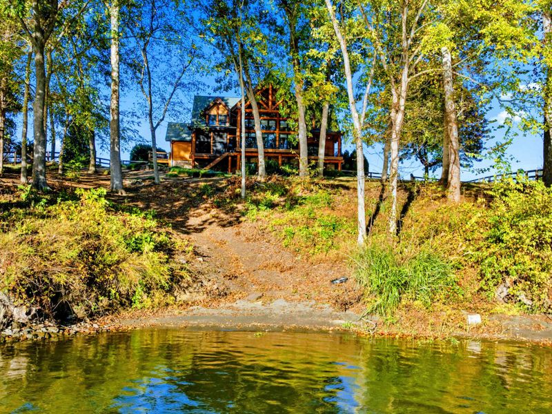 Waterfront - View from the lake looking back at the wooded shoreline with the timber frame home visible through mature hardwoods.