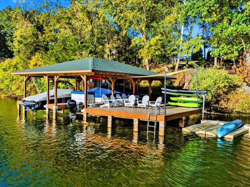 Aerial - Spacious dock with bar-height seating, kayaks on shore, and the boathouse viewed from the water.