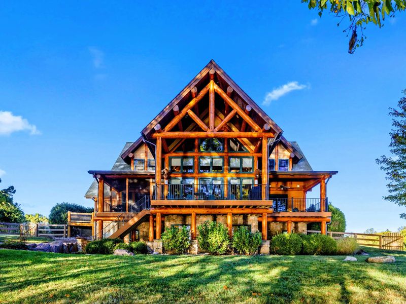 Exterior - Stunning timber frame and log home with soaring A-frame peaks, exposed beams, and a stone base set against a blue sky.