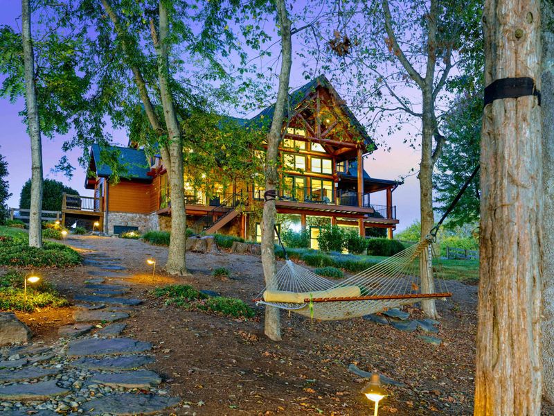 Exterior - The timber frame home glows at twilight with landscape lighting illuminating the stone pathway and a hammock in the foreground.