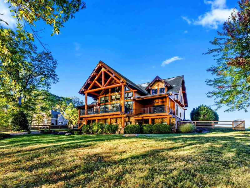 Exterior - Side view of the timber frame home showcasing the upper balcony, log construction, and expansive green lawn.