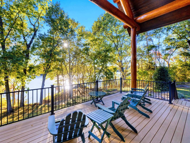 Deck - Green Adirondack chairs and lounge seating line the expansive deck overlooking the lake through the trees.